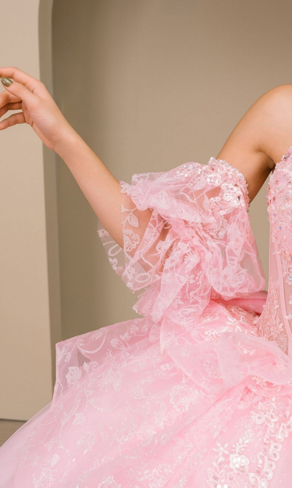 A person is wearing the Quinceanera Dress 8535JQ by Cinderella Couture, featuring pink lace and tulle with sheer, ruffled sleeves. Only the upper torso and left arm are visible against a plain background.